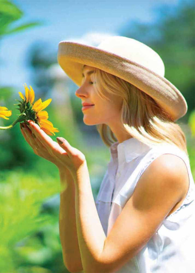 Up brim hats are flattering for women. Bring a little up lift and happiness. women in beige knit up brim hat smelling a sun flower