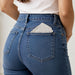 Close-up back view of a person wearing blue denim jeans with a white Scrunchie hat inserted in the back right pocket.